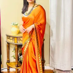 A client looking radiant in a vibrant orange saree. She styled it with a long, multi-layered traditional necklace that adds a touch of heritage and grace to her look.