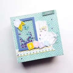 Celebrating a new arrival is pure joy. This is the cover of a baby scrapbook, designed with a fun shaker window filled with colorful sequins and cute "BABY" blocks to mark the beginning of a beautiful new story.