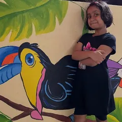 A young admirer posing proudly next to the toucan mural, showing how this art can brighten up a space for the whole family.