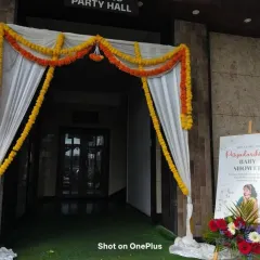 A simple and traditional entrance for a baby shower. The doorway is decorated with marigold garlands and white drapes, with a welcome easel board placed to the side.