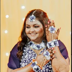 A smiling bride adorned with floral jewelry, showing off her dark and detailed mehendi. Her happiness is infectious.
