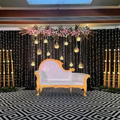 This sangeet stage combines a black fairy light backdrop with a modern geometric floor pattern. The elegant floral arrangements and hanging glass globes add a touch of softness to the contemporary design.