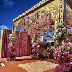 A vision in blush pink and gold. This mandap at JW Marriott Bangalore Golfshire features intricate golden panels and suspended floral strings, creating a space that feels both regal and romantic under the open sky.