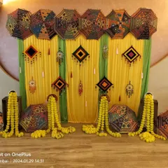 This is a classic Gujarati and Rajasthani style Mehndi decor. We use colorful embroidered umbrellas, wall hangings, and marigold garlands against a bright yellow and green backdrop.