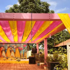 A wider angle of the outdoor Haldi venue, showing the pink and yellow fabric canopy that provides shade and color to the event.