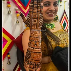 A smiling bride proudly displaying her intricate bridal mehendi. The design features personalized initials and traditional motifs, looking beautiful against her festive attire.