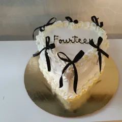 A chic and trendy heart-shaped cake for a fourteenth birthday. The minimalist design with black ribbons is a modern take on the classic celebration cake.