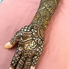 A close-up showing beautiful Arabic calligraphy integrated into the palm of a full bridal mehendi design.