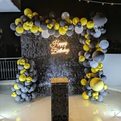 A direct shot of the black sequin backdrop, highlighting the contrast with the bright yellow and grey balloons and the warm glow of the neon sign.
