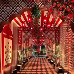 A lavish cultural-themed entrance, with a passageway defined by red and white patterned walls, checkered flooring, and ornate red chandeliers, evoking the feeling of walking through a royal Indian palace.