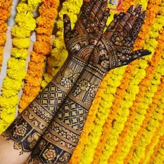 A gorgeous full bridal mehndi set against a backdrop of marigold flowers. The design features traditional bands of geometric and floral patterns, perfect for a wedding ceremony.