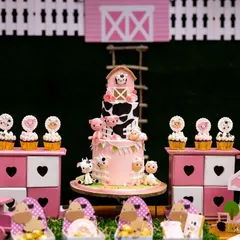 The dessert table is the heart of our barnyard theme. It features a stunning multi-tiered farm animal cake, surrounded by adorable sheep cupcakes and themed treat boxes, all displayed on custom-built stands.