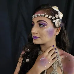 This mermaid look features iridescent purple tones and a subtle scale texture on the skin. The look is completed with carefully placed pearls on the face and body for an ethereal, underwater feel.