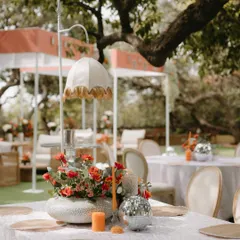 A whimsical and charming table centerpiece, featuring a vintage-style lamp, a vibrant orange floral arrangement, and a mini disco ball, perfectly capturing the fun and stylish spirit of the event.