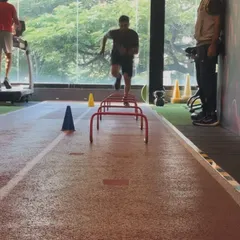 A client performs agility drills over hurdles under the watchful eye of a coach, perfecting his movement patterns.
