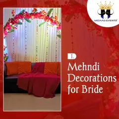 This is a classic and comfortable seating arrangement for the bride during her Mehndi ceremony. A sofa with bright cushions is placed under a beautiful arch of pink flowers and hanging crystal strings, creating a rich and elegant look.