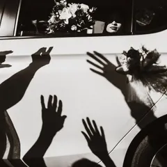 A creative use of shadows during the bride's departure. The hands waving goodbye are projected onto the car, creating a powerful and artistic farewell image.