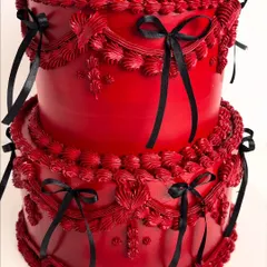 A close-up of the intricate, hand-piped detailing on our bold red "Scorpio Baby" cake. The vintage-style piping and black ribbon accents create a dramatic and luxurious texture.