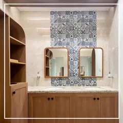 In the ladies' washroom, a feature wall of patterned blue tiles provides a vibrant contrast to the warm wood cabinetry and colonial gold stone countertops. The custom-framed mirrors with rounded corners soften the space, blending classic and contemporary design elements.