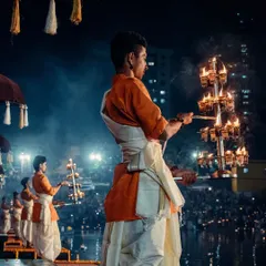 Another angle of the priest holding the ceremonial lamp, with the crowd of devotees visible in the background, highlighting the shared experience of the Dev Deepawali festival.