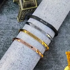 I offer these sleek name bracelets, or kadas, in a variety of finishes to match any style. This image shows the range, including rose gold, classic gold, silver, and modern matte black, each engraved with a name.