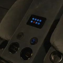 A close-up of the smart panel integrated into the recliner's center console. The matte black finish and illuminated icons add to the high-tech, luxurious feel of the theater.