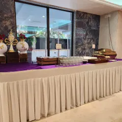 A section of a buffet table featuring elegant decor pieces, neatly arranged glassware, and premium chafing dishes. The purple and white theme adds a touch of royalty to the setup.