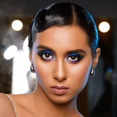 This shot captures the full effect of the electric blue eye makeup against the studio lights. The clean, sculpted brows and flawless skin provide the perfect canvas for such a strong, color-focused editorial statement.