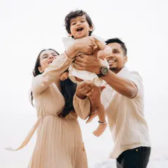 Pure happiness as parents lift their laughing baby into the air during a bright day at the beach. This photo is all about capturing the energy and delight of candid child photography.