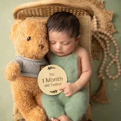 One month of sweetness. This little one is sleeping so peacefully next to his teddy bear, holding a sign to mark his first big milestone.