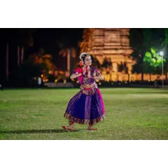 A dancer performs a Bharatanatyam piece on a lawn at dusk, with an illuminated temple in the background. This shot demonstrates my use of ambient and artificial light to create a serene and visually rich performance photograph.