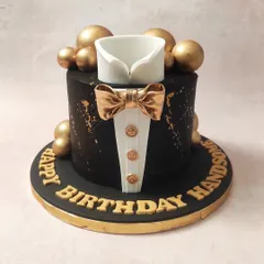 We present the essence of formal sophistication with our black and gold tuxedo cake. This design features a sharp, edible shirt collar and a lustrous gold bow tie set against a matte black tier, accented with gold splatters and spheres, making it an impeccable choice for a gentleman's milestone birthday.