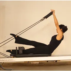 A client performs a teaser variation with feet in straps on the reformer. This move deeply engages the core while also working the legs and arms.