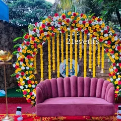 A bright and cheerful outdoor setup for a pre-wedding event. The circular arch is heavily decorated with yellow, red, and white flowers, complemented by hanging marigold strings.
