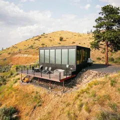 This modern cabin with a spacious deck and integrated hot tub is designed for ultimate relaxation. The large glass panels offer panoramic views, seamlessly blending the indoor living space with the surrounding landscape.