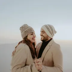 A happy couple, dressed in cozy winter wear and beanies, shares a laugh against the soft, hazy backdrop of the Himachal mountains. This candid moment captures the warmth of their connection in a cold climate.