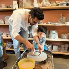 A father gently guides his son's hands on the potter's wheel. Our family workshops are designed to be a bonding experience, creating a space for connection and shared creativity.