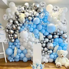 A classic 'Baby Boy' baby shower wall decoration. The dense balloon wall in shades of blue, silver chrome, and white creates a stunning backdrop, complete with a teddy bear and a pedestal for gifts or a cake.