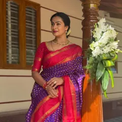 A client radiating elegance in a classic red and purple combination. The simple yet signature jewellery motif on the elbow-length sleeves adds a touch of sophistication without overpowering the Kanjivaram saree.
