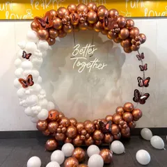 A stylish balloon ring decoration with a 'Better Together' neon sign, perfect for an engagement party or anniversary. The arrangement uses on-trend chrome copper and white balloons with butterfly accents.