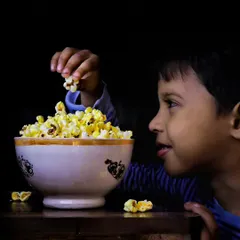 A candid portrait of my son enjoying a bowl of popcorn, captured with dramatic lighting to highlight his expression. These are the *mera bachcha* moments that I love to freeze in time.