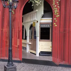 A view of the Soley Cafe entrance framed by a bold, red slatted screen. This contrast between the modern red structure and the vintage-inspired cafe facade creates a dynamic and visually interesting entryway.