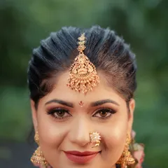 A beautiful close-up portrait of a model in a South Indian bridal look. Her expressive eyes and traditional gold jewelry, including the maang tikka and nath, are the centerpiece of this shot.
