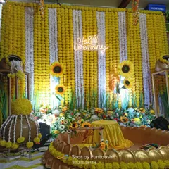 A vibrant Haldi stage with a backdrop of yellow and white marigold strings, a neon 'Haldi Ceremony' sign, and a unique lotus-shaped seat for the bride.