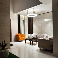 An elegant living space featuring a mix of textures, from the polished marble floor and wood-paneled wall to the soft furnishings and modern ring chandelier.