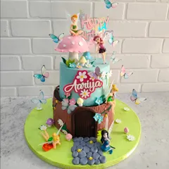 A closer look at our fairy garden cake. This two-tier cake features a whimsical fairy house design, complete with a fondant door, a mushroom on top, and tiny, delicate butterflies.