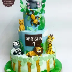 A three-tier jungle animal theme cake for a first birthday. This design features adorable, hand-molded fondant animals like a lion, giraffe, and elephant, set against a vibrant jungle backdrop.