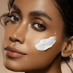 This portrait captures the result of a good skincare routine. The model's clean, glowing skin and direct gaze convey confidence. The smear of cream on her cheek is a visual cue that tells the story of the product's texture and application in a single, elegant frame.