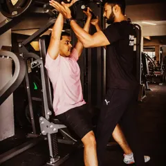 My role as a coach is to guide and push you safely. Here, I'm spotting a client during a shoulder press, ensuring correct form and providing the support needed to maximize the lift and prevent injury.