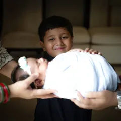 A creative and heartwarming portrait showing a newborn being held by their parents' hands, with their proud older brother smiling in the background. This photo beautifully symbolizes the family's circle of love.
